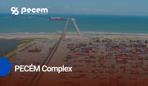 An aerial view of the PECÉM Complex, showcasing a busy port with shipping containers and a long pier extending into the ocean, highlighting industrial and logistical operations.